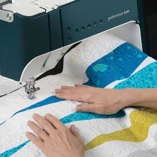 Two hands guide a vibrant quilt under a sewing machine, demonstrating curved blue, yellow, and white patterns in the Machine Quilting Freemotion Class by Quilted Joy.