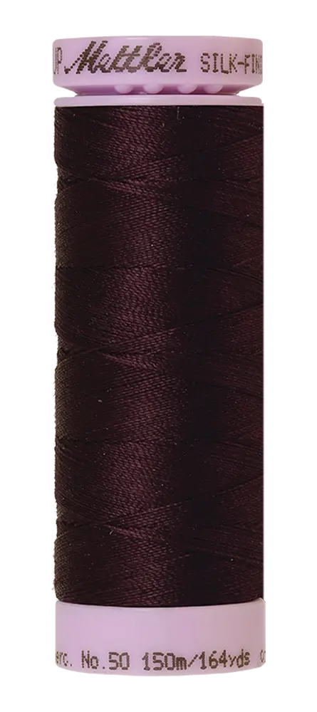 A spool of Mettler Cotton Silk Finish 50wt in "Plum Perfect" (150m) is ideal for quilting or cotton sewing projects, wound on a light pink plastic spool labeled “Mettler Silk-Finish.”.