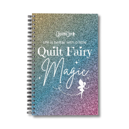 The Quilt Fairy Magic Notebook by quiltedjoy is a spiral-bound notebook with a glittery rainbow cover, “Life is better with a little Quilt Fairy Magic” text, and fairy art—a perfect gift for quilters to record their notes.