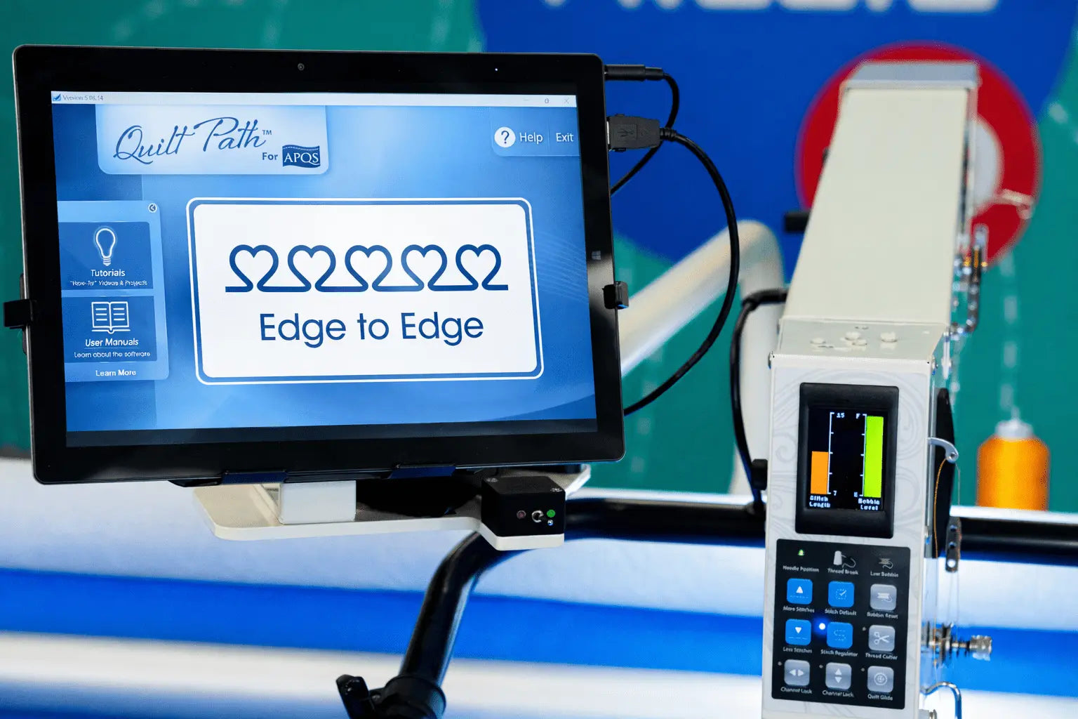 A digital screen shows “Edge to Edge” with five linked hearts on the APQS Quilt Path Robot Computer by APQS, featuring a control panel with buttons and a small color display for precise computerized quilting.