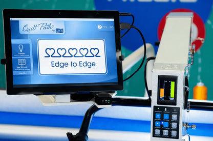 A digital screen shows “Edge to Edge” with five linked hearts on the APQS Quilt Path Robot Computer by APQS, featuring a control panel with buttons and a small color display for precise computerized quilting.