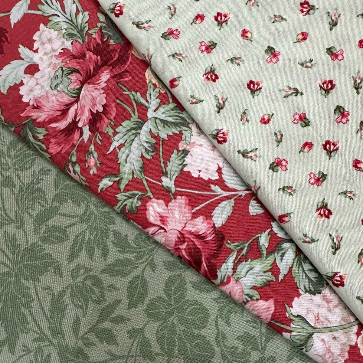 The Quilted Joy Regal Rose 3 Yard Quilt Top Bundle includes three 100% cotton fabrics: bold pink flowers on red, small pink blooms on cream, and a subtle green leafy print—ideal for pairing with Fabric Cafe 3-yard quilt books.
