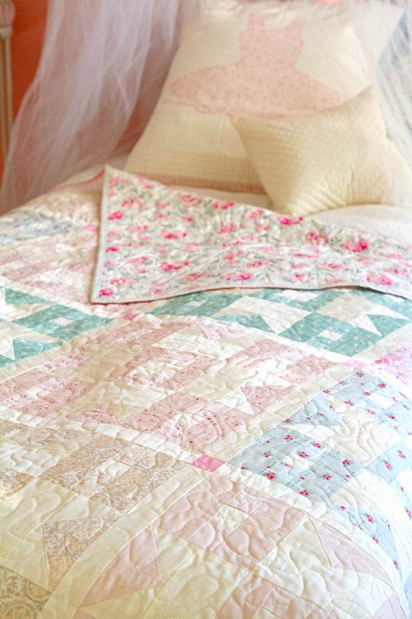 A bed styled with the Romantica Half Yard Bundle features a pastel patchwork quilt and matching pillow in soft pink, blue, and cream florals, creating a light, cozy, and feminine look.