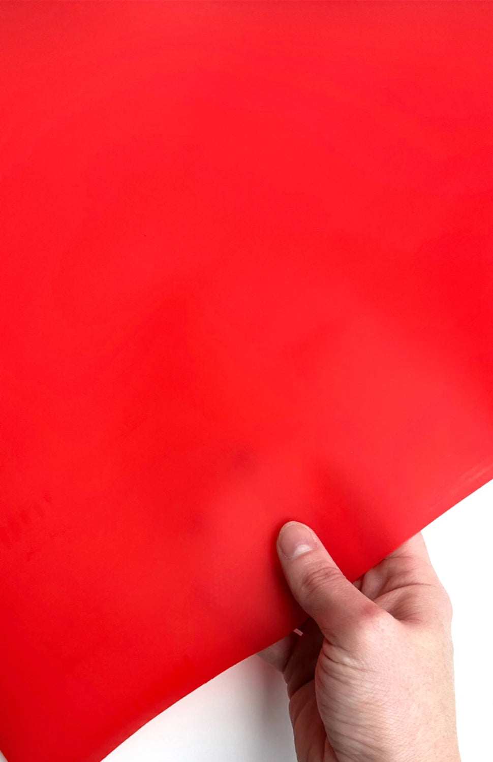 A hand holds the corner of a Checker Distributor Red Jelly Vinyl 18" x 53" sheet against a white background.