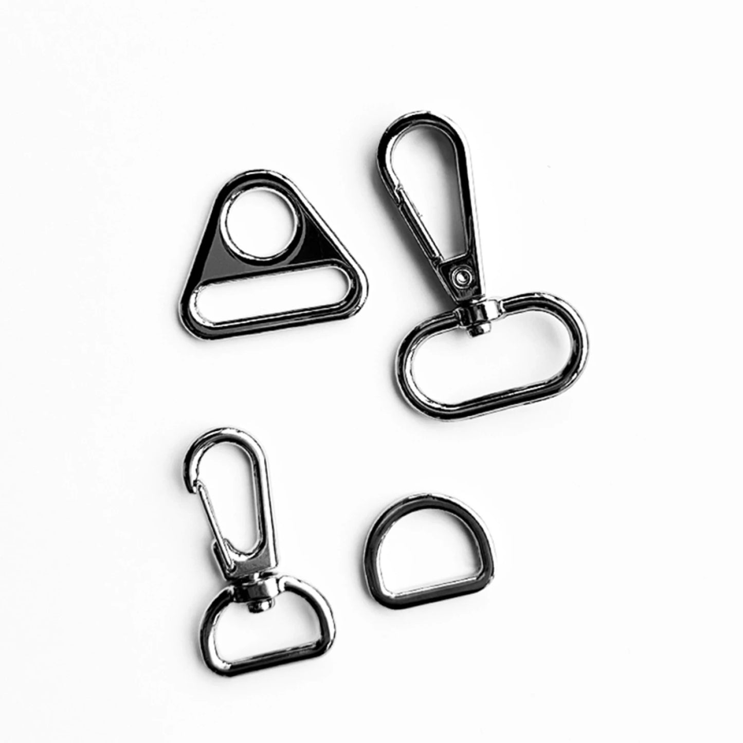 Four shiny silver purse hardware pieces from Checker Distributor’s Quick Boxy Pouch Hardware Kit—a triangular ring, two swivel hooks, and a D-ring—perfect for your next project.