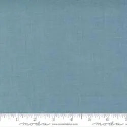 A square sample of French General French Blue Solids Fabric Yardage by United Notions, featuring a subtle texture. A white Moda Fabrics–branded ruler shows inch measurements along the bottom—ideal for quilting projects.
