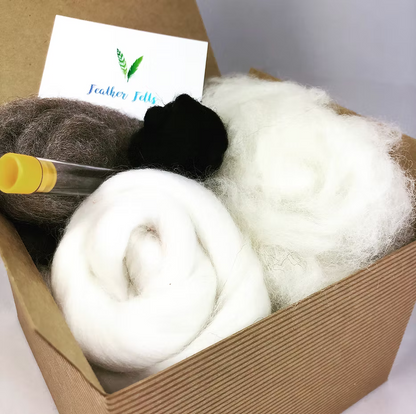 The Grey Sheep - Needle Felting Kit No Foam by Feather Felts includes rolled white wool, a dark brown ball, a small black bundle, a clear tube, and a Feather Felts business card—ideal for beginner needle felting projects.