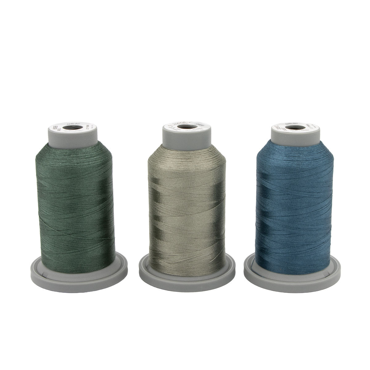 Three large spools of Hab+Dash by Fil Tec Stormy Sprite Glide Thread of the Month Bundle in green, beige, and blue are arranged in a row on a white background. Each quilting thread spool has a gray plastic base.