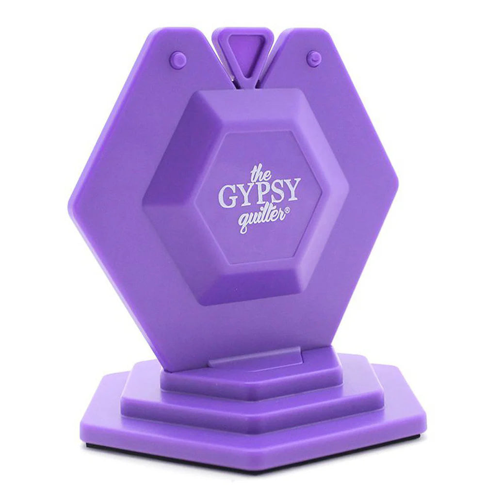 The Chain Piece Thread Cutting Gizmo by Tacony Corporation is a purple, hexagon-shaped thread cutter with top slots for easy thread insertion, resting on a matching base—perfect for cutting threads during your sewing projects.