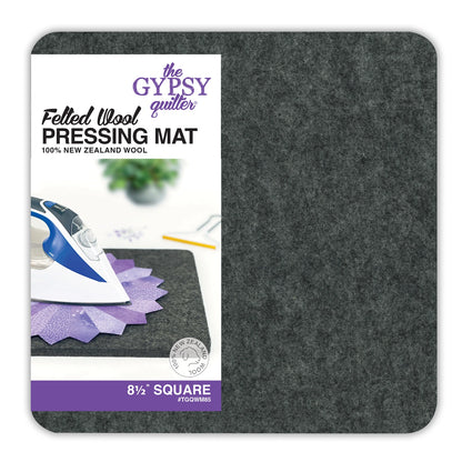A gray Wool Pressing Mat by Checker Distributor, 8-1/2" square and 1/2" thick, is shown with packaging. An iron and a purple quilt piece rest on this ideal pad for quilting projects.
