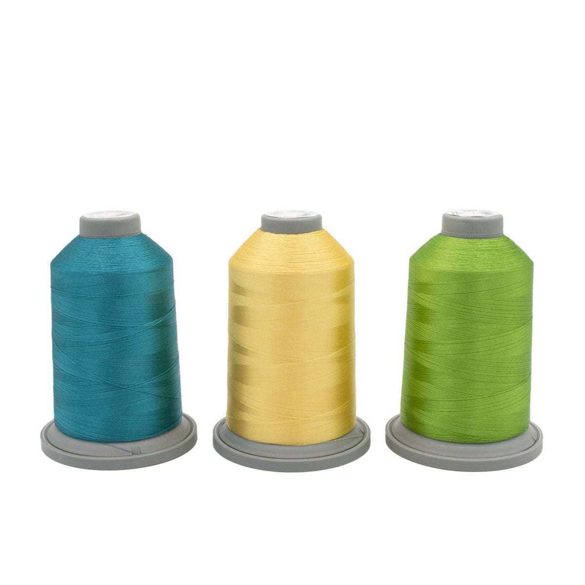 Three large spools from the Topaz Tropics Glide Thread of the Month Bundle by Hab+Dash by Fil Tec in teal, yellow, and green, ideal for embroidery or quilting, displayed upright on a gray base against a white background.
