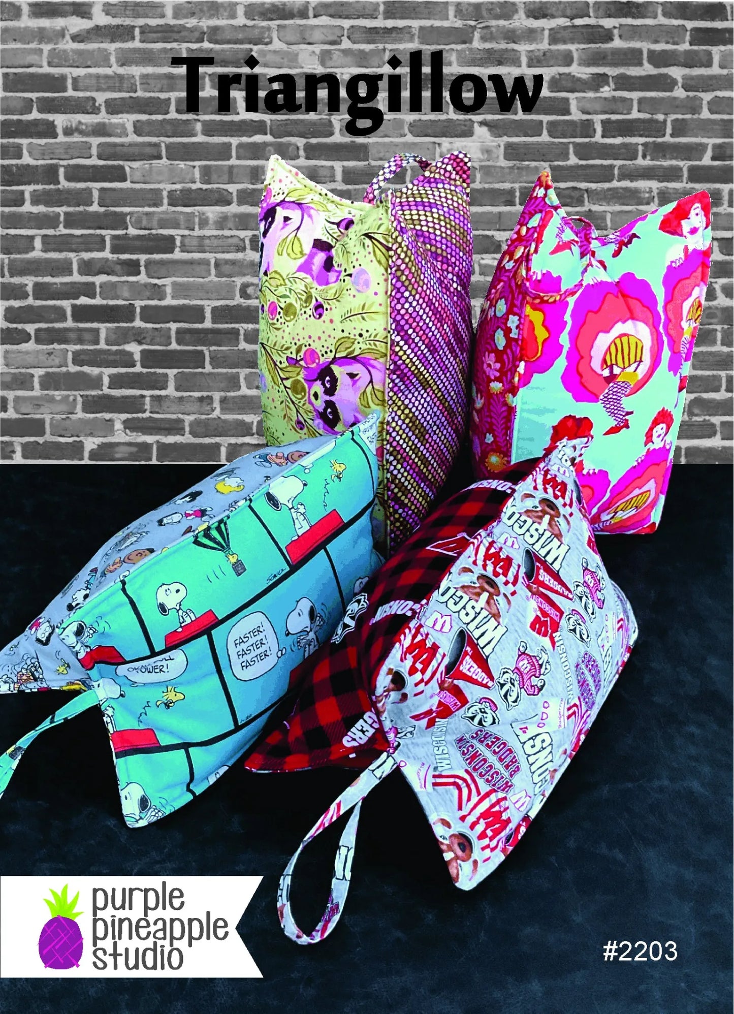 Five vibrant, triangular fabric bags with handles stand against a brick wall, each showcasing playful designs made with the Triangillow Quilt Pattern by Purple Pineapple Studio. The text reads Triangillow and #2203.