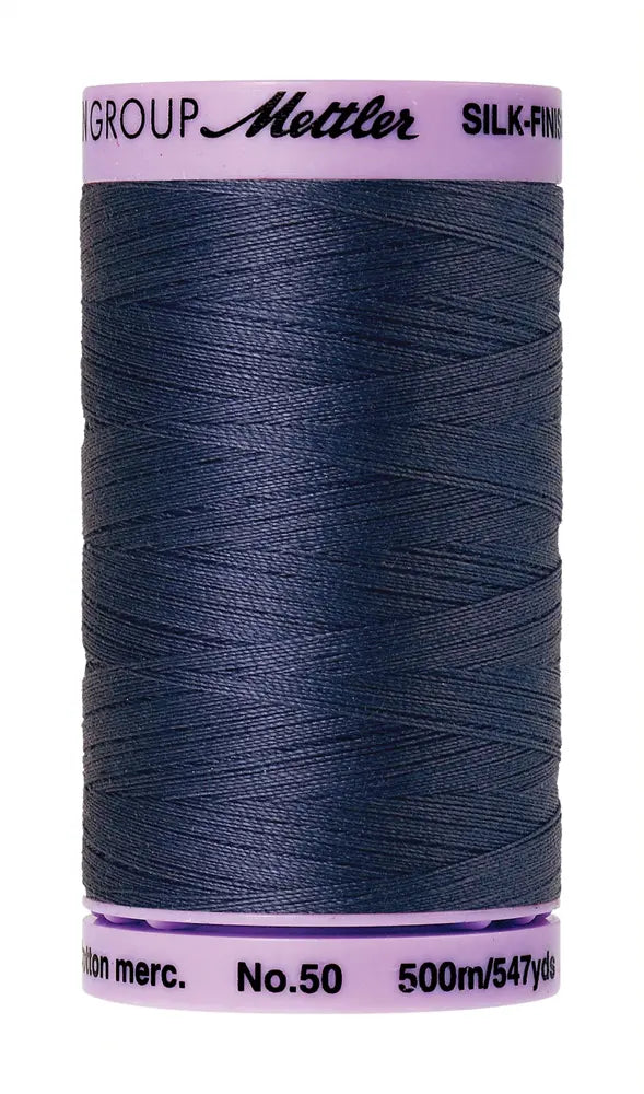 A spool of Mettler Cotton Silk Finish 50wt 500m in True Navy, featuring a light purple label—ideal as a versatile cotton sewing or dependable quilting thread.