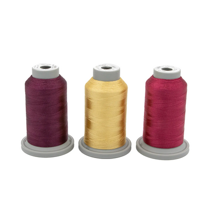 The Velvet Vineyard Glide Thread of the Month Bundle by Hab+Dash features three upright spools in purple, yellow, and reddish-pink on gray bases—perfect for embroidery or quilting and adding vibrant color to your projects.