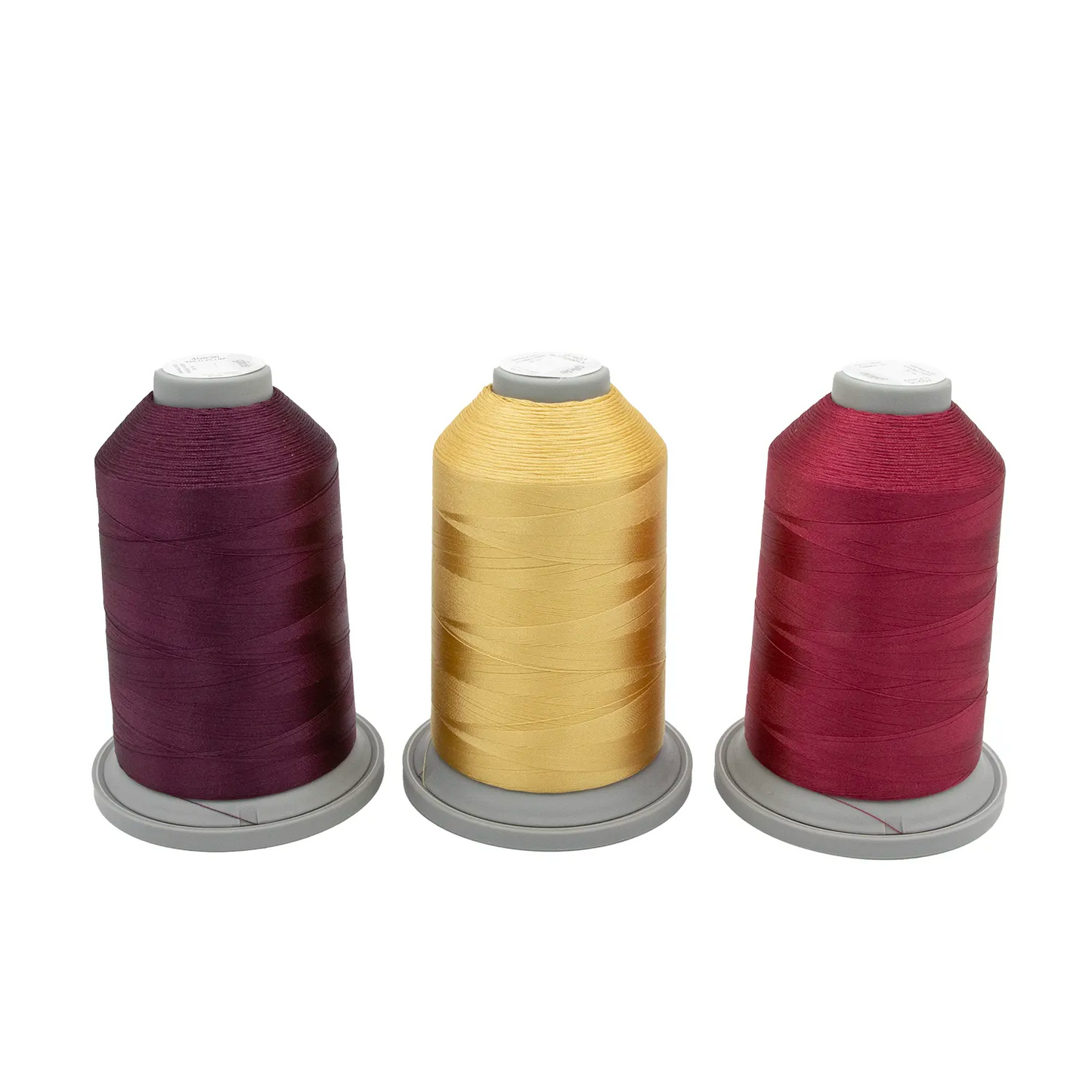 Three large spools from the Velvet Vineyard Glide Thread of the Month Bundle by Hab+Dash by Fil Tec—one dark purple, one yellow, one red—stand upright on gray bases against a white background, ideal for embroidery or quilting.