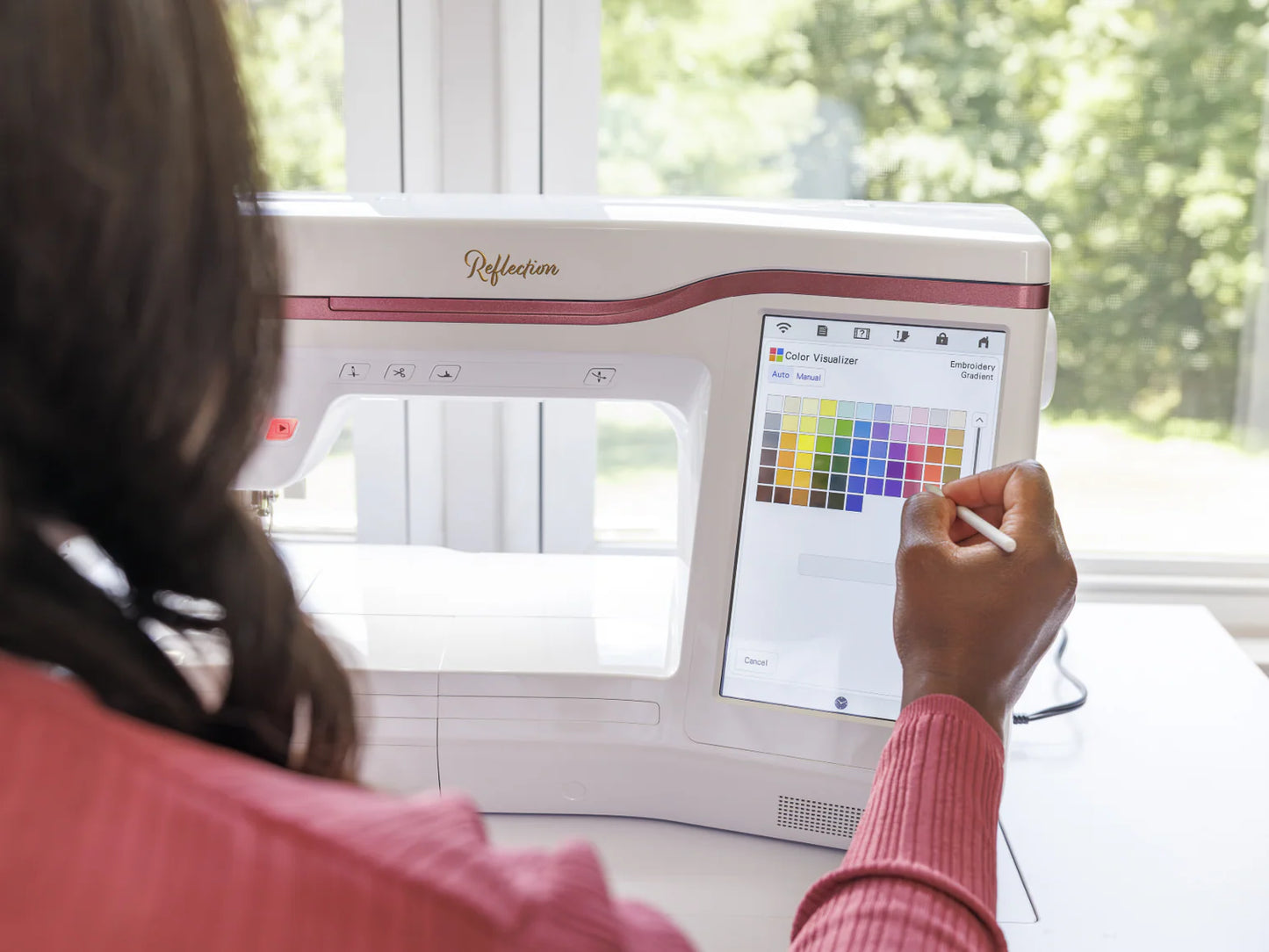 A person uses a stylus to pick colors on the touchscreen of the Baby Lock Reflection Sewing & Embroidery machine with FREE 60 Days of Online Classes, sunlight and greenery visible through the window—ideal for creative projects with its large embroidery field.