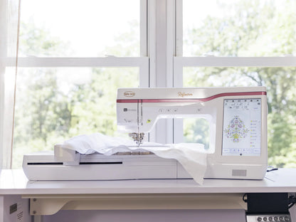 A Baby Lock Reflection Sewing & Embroidery machine with FREE 60 Days of Online Classes sits by a sunny window, stitching a bright floral pattern on white fabric while its digital touchscreen displays the large embroidery area.