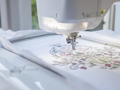 A close-up of the Baby Lock Reflection Sewing & Embroidery Machine with FREE 60 Days of Online Classes stitching a colorful floral and bird design, highlighting its large embroidery field for intricate leaves, flowers, and lines.