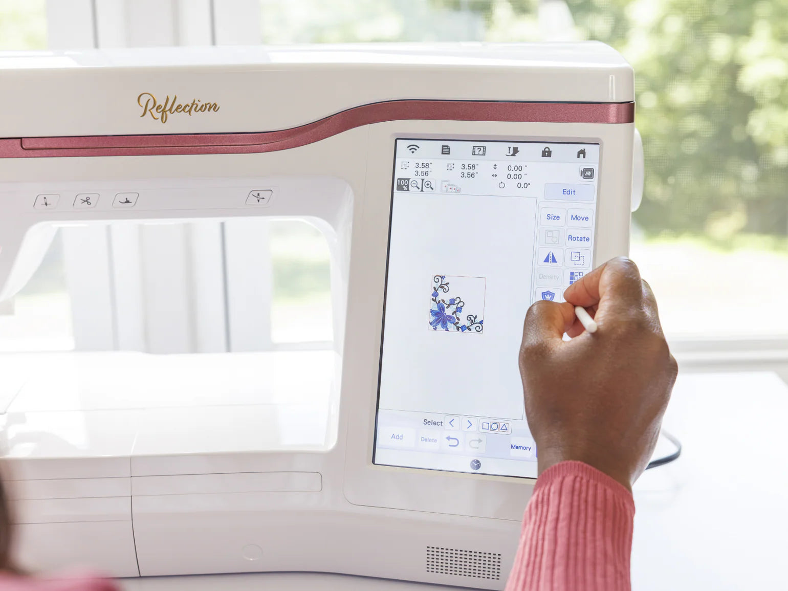 A user interacts with the Baby Lock Reflection Sewing & Embroidery machine’s touchscreen, choosing or editing a floral design in its large embroidery field. Sunlight pours through a window behind. Includes FREE 60 Days of Online Classes.