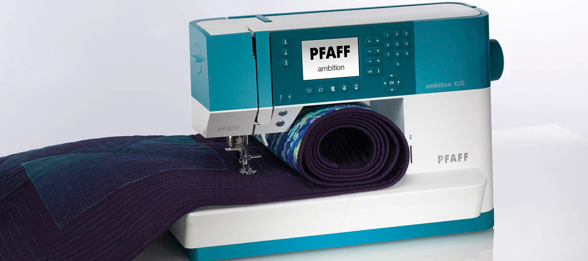 A turquoise and white Pfaff Ambition 620: PRE-LOVED by Quilted Joy is quilting a dark, geometric-patterned fabric, with the material partially beneath the needle and extending to the side.