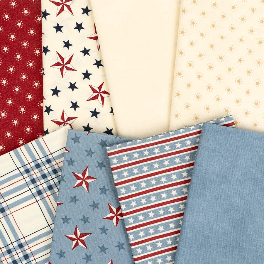 Seven pieces from the United Notions America 250 Years Mini Charm Pack in red, white, and blue with stars, stripes, plaid, and dot patterns are artfully fanned out and overlap each other.