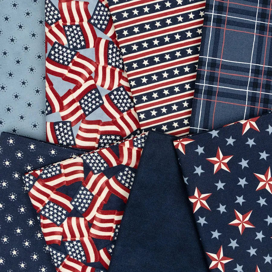 Red, white, and blue fabric squares from the United Notions America 250 Years Mini Charm Pack—featuring flags, stars, stripes, plaid, and solids—are arranged overlapping on a flat surface.