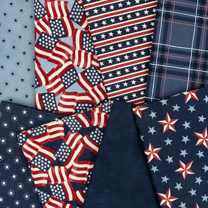 Red, white, and blue fabric squares from the United Notions America 250 Years Mini Charm Pack—featuring flags, stars, stripes, plaid, and solids—are arranged overlapping on a flat surface.