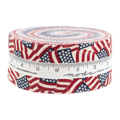 The America 250 Years Jelly Roll by United Notions features rolled fabric strips with overlapping American flags, wrapped in a white measuring tape-printed ribbon and branded with “moda.”.