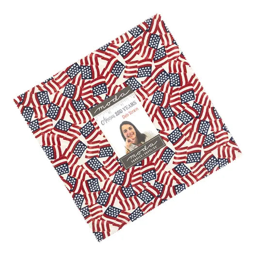 The America 250 Years 10" Layer Cake by United Notions features quilting fabric with small American flags, celebrating America's 250th anniversary. The center label reads “Moda,” “Independence Trail,” and has a photo of a woman.