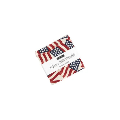 A stack of fabric squares from the United Notions America 250 Years Mini Charm Pack, featuring an American flag pattern and wrapped with a label reading "America 250 Years by Deb Strain.