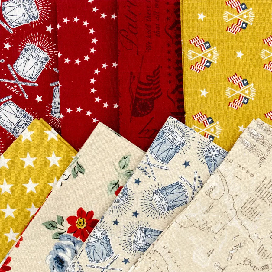 The Independence Fat Quarter Bundle by Riley Blake features patterned fabric swatches in red, yellow, cream, and blue with stars, drums, American flags, florals, and vintage maps—perfect for quilting projects.