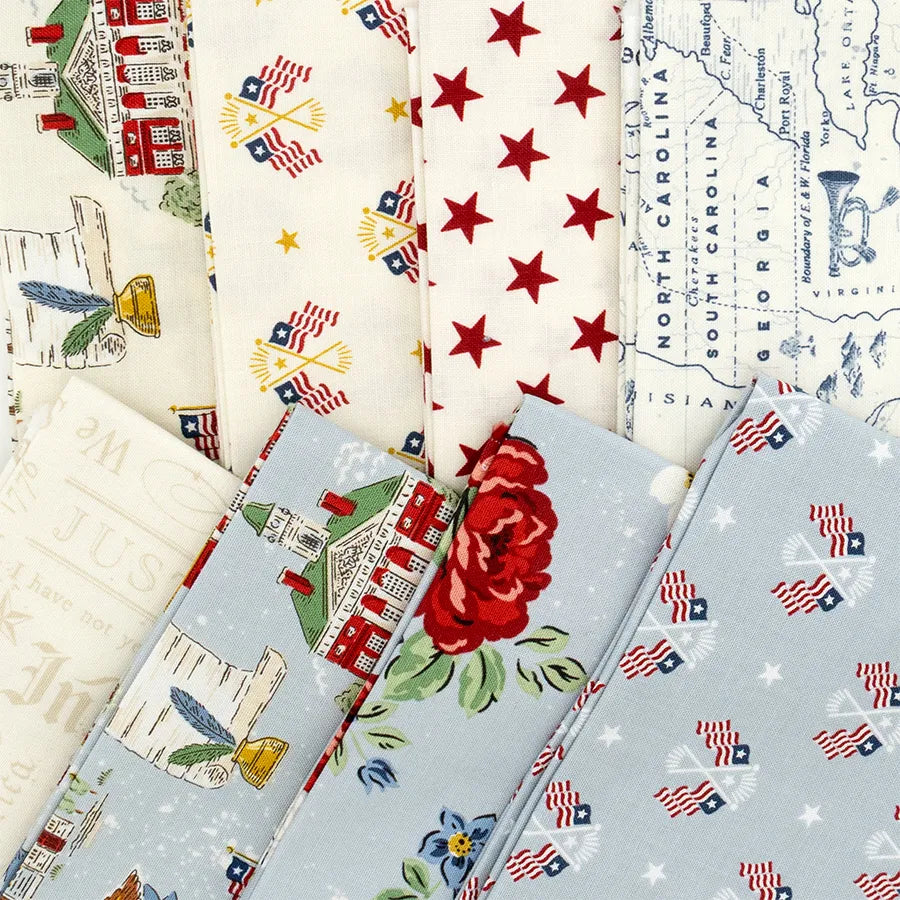 The Independence Fat Quarter Bundle by Riley Blake features patterned fabrics with American flags, red stars, vintage houses, maps, roses, quills, and books in patriotic colors—perfect for quilting projects.