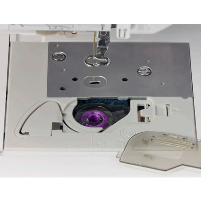 Close-up of the Baby Lock Flare Dedicated Embroidery Machine with FREE Online Classes, highlighting its bobbin case, metal needle plate, purple plastic bobbin, and a partially open transparent cover.