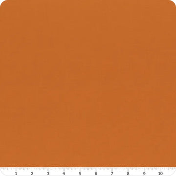 A square of Riley Blake Confetti Cotton™ Amber Solid Fabric with a subtle texture is shown, featuring a white ruler along the bottom from 0 to 12 inches. The fabric’s rounded corners make it perfect for quilting and other cotton projects.
