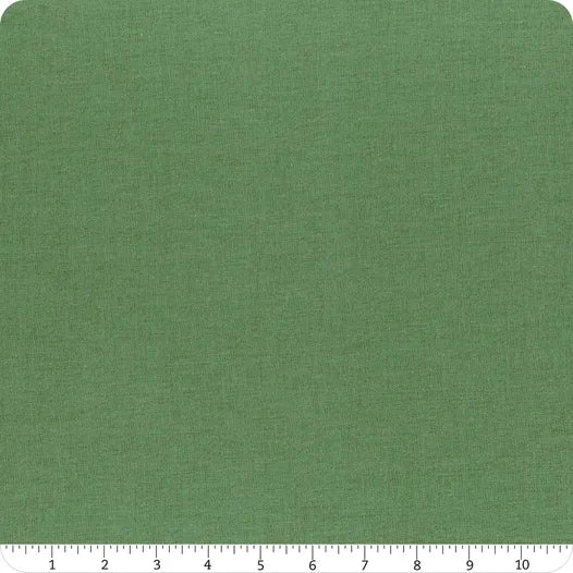 A square piece of Confetti Cotton™ Lodge Pole Solid Fabric by Riley Blake is shown against a white background with a ruler below (0–11 inches) for scale. The green fabric has a subtle texture and slightly rounded corners.