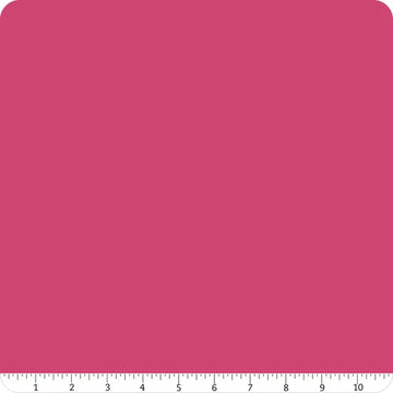 A square swatch of Confetti Cotton™ Riley Fuchsia Solid Fabric Yardage by Riley Blake with rounded corners. A white ruler marked 1 to 10 in black runs along the bottom edge for scale.