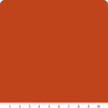 A square of solid reddish-brown fabric with rounded top corners. Along the bottom edge, a white ruler from 1 to 10 inches shows the scale of this Riley Blake Confetti Cotton™ Rusty Solid Fabric Yardage, perfect for quilting projects.