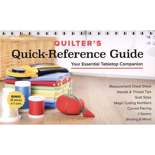 A tabletop holds folded fabric, thread spools, scissors, and a tomato pincushion. The cover reads: Quilter's Quick-Reference Guide by Checker Distributor—your essential resource for quilt block diagrams and tips.