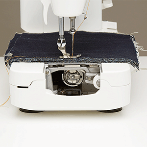 The JUKI Haruka TL-18QVP sewing through a folded stack of heavy dark denim, with the free arm and bobbin area visible.