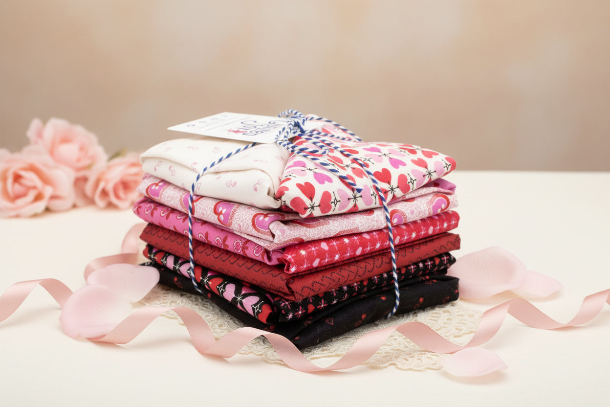 A stack of Heart and Soul Fat Quarter Bundle by Andover in pink, red, and black floral and heart prints, tied with blue-and-white string—ideal for quilting projects.