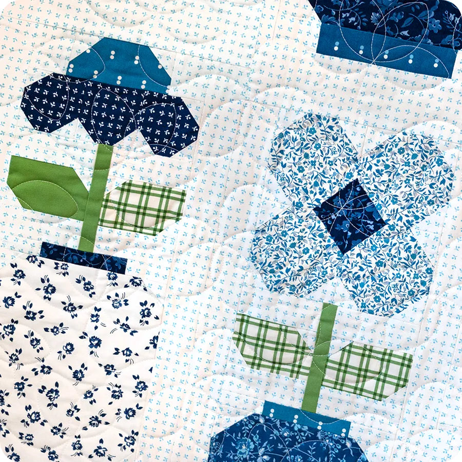 The Blueprint Quilt Kit by United Notions features quilted fabric with blue and white floral vase patterns, green leaves and stems, plus a light background with blue dots—design inspired by Camille Roskelley and Ginger Jars Quilt Pattern.