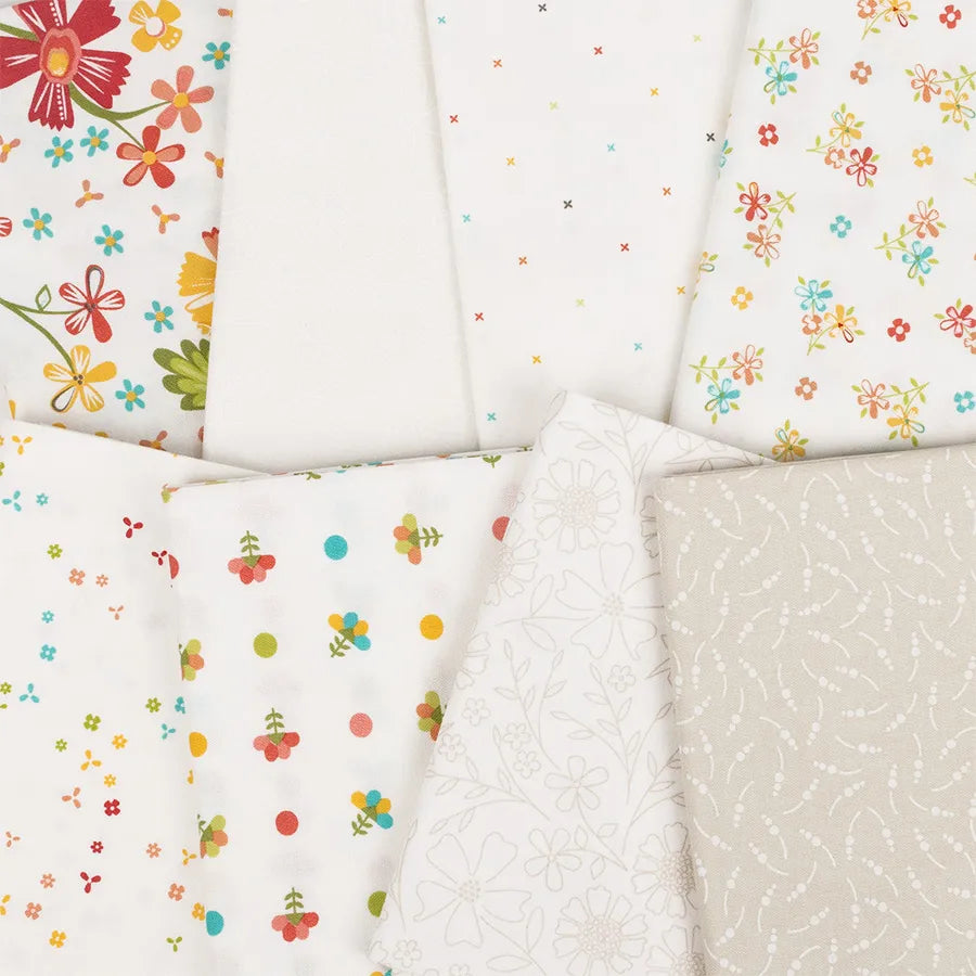 An arrangement of seven fabric pieces from the In The Garden Mini Charm Pack by United Notions, featuring colorful flowers, small dots, cherries, and subtle white-on-white floral and swirl patterns on mostly white backgrounds.