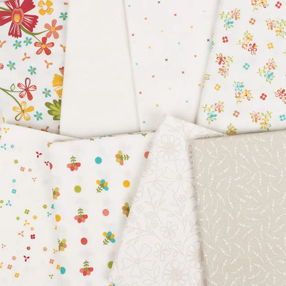 An arrangement of seven fabric pieces from the In The Garden Mini Charm Pack by United Notions, featuring colorful flowers, small dots, cherries, and subtle white-on-white floral and swirl patterns on mostly white backgrounds.