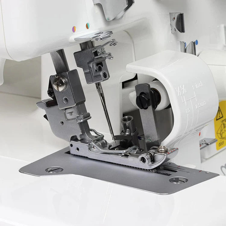 Close-up of the Juki America Pearl Line MO-655 2/3/4/5 Thread Serger’s needle area, highlighting the presser foot, needle, feed dogs, and threading mechanism with distinct metal and plastic parts.