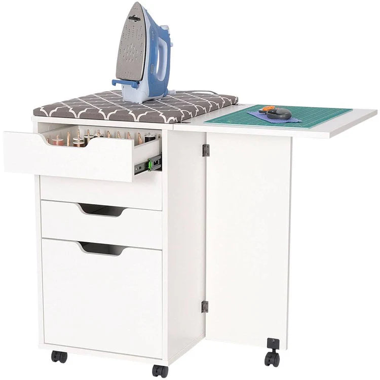 The Kiwi Multi-Use Cabinet is versatile sewing furniture on wheels, with a spacious cutting surface, ironing board, green cutting mat, open drawers for thread spools, and a convenient fold-out side table.