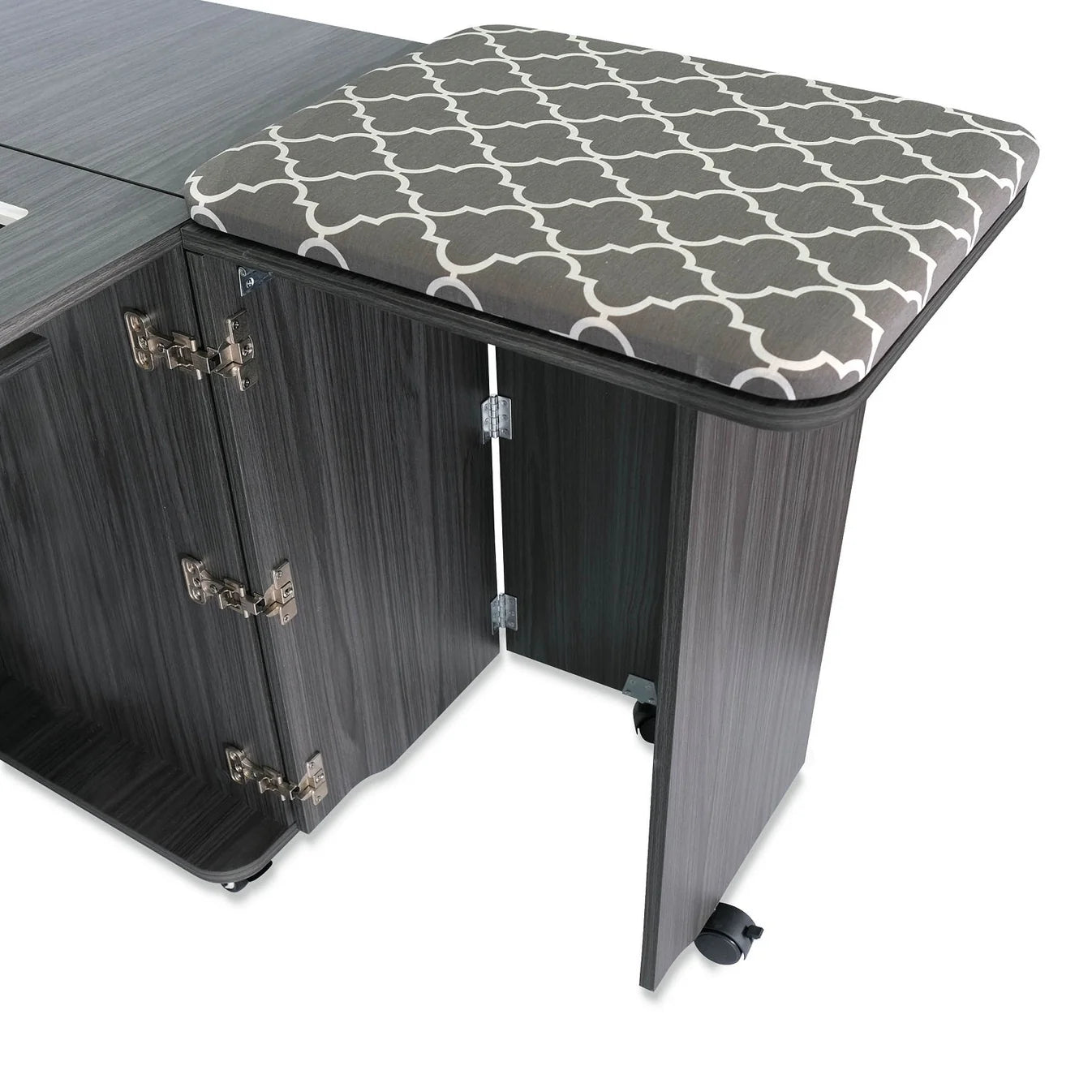 A cushioned stool with a gray and white geometric pattern is partially tucked under the Arrow Companies, LLC Kangaroo Sydney Sewing Cabinet with Electric Lift, which features multiple hinges and caster wheels.