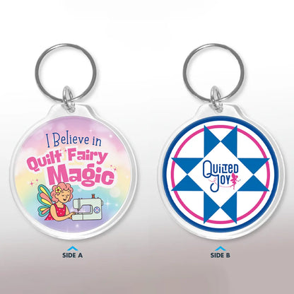 The Checker Distributor Quilt Fairy Magic Keychain features a fairy by a sewing machine with "I Believe in Quilt Fairy Magic" on one side and a blue quilt star with "Quilted Joy" on the other—a delightful accessory for quilting enthusiasts.