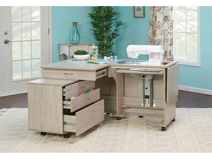 The Koala Quilters Vision Sewing and Companion Chest in White and Gray holds a white sewing machine, art supplies on top, and sits in a bright room with teal walls and large windows.