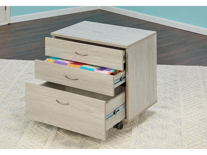 The Koala Quilters Vision Sewing and Companion Chest in White and Gray with three drawers on wheels sits on a textured rug. Two drawers are open, showing a colorful quilt. The cabinet is in a blue-walled room with dark floors.