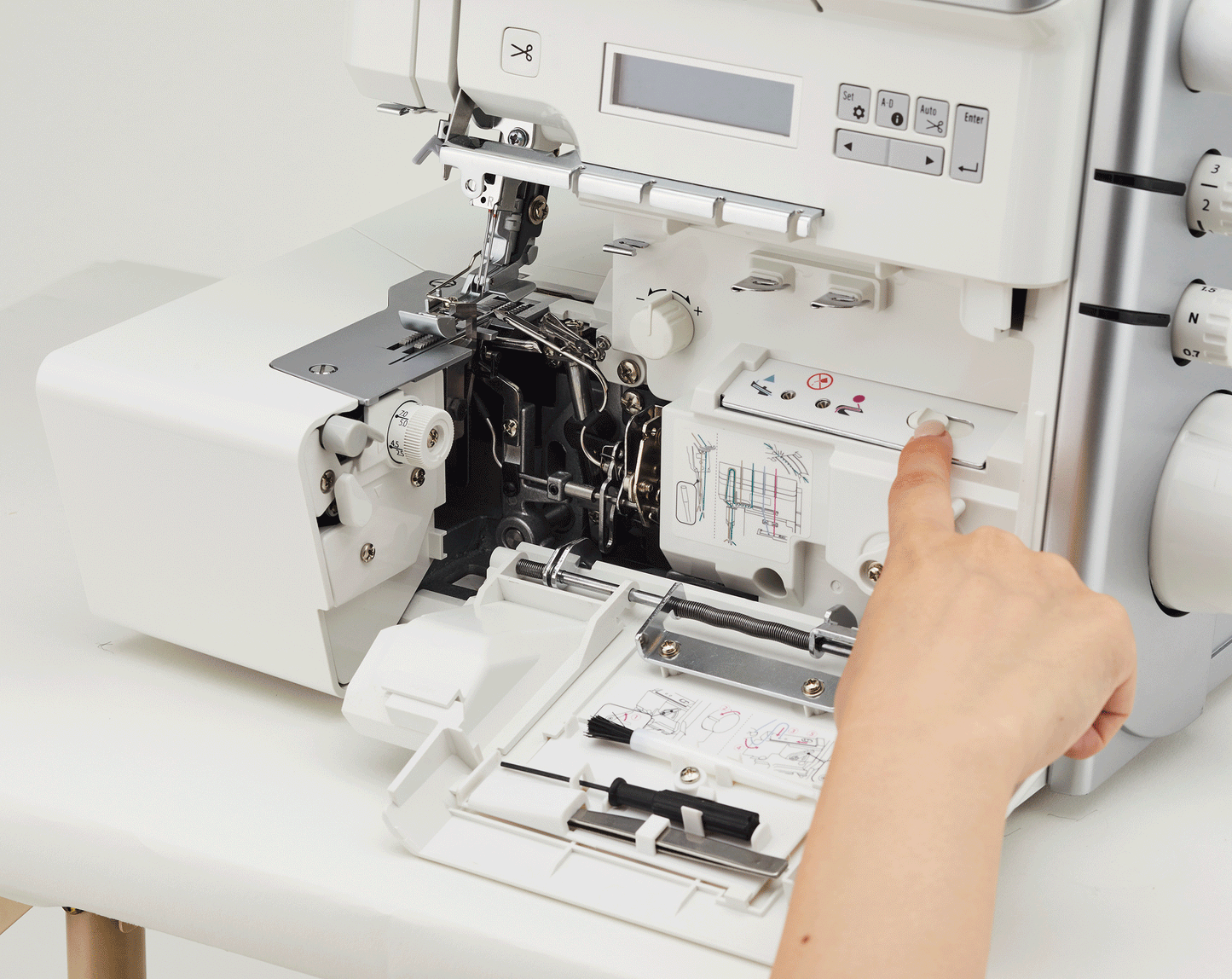 The front cover of the JUKI Akane MO-3000QVP swung open to show the looper area and the threading diagram printed inside, with a finger on the air threading button.